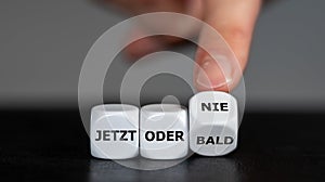 Hand turns dice and changes the German expression `jetzt oder bald` now or soon to `jetzt oder nie` now or never. photo