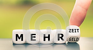 Hand turns dice and changes the German expression `mehr Geld` `more money` to `mehr Zeit` `more time`.