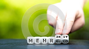 Hand turns dice and changes the German expression `mehr Geld` more money to `mehr Zeit` more time.
