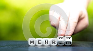 Hand turns dice and changes the German expression `mehr Geld` more money to `mehr Zeit` more time. photo