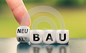 Hand turns a dice and changes the German word `Altbau` `old construction` in English to `Neubau` `new construction` in