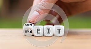 Hand turns a dice and changes the German word `Arbeit` `work` in English to `Freizeit` `leisure time` in English photo