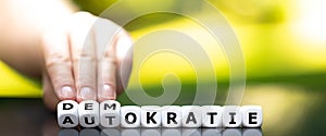 Hand turns dice and changes the German word `Autokratie` autocracy to `Demokratie` democracy.