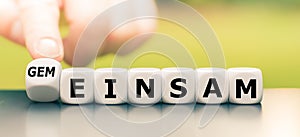 Hand turns a dice and changes the German word `einsam` `lonely` in English to `gemeinsam` `together` in English.