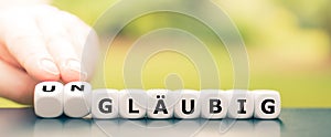 Hand turns dice and changes the German word `glÃ¤ubig` religious to `unglÃ¤ubig` irreligious.