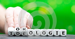 Hand turns dice and changes the German word `Ideologie` ideology to `Ã–kologie` ecology.