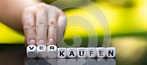 Hand turns dice and changes the German word `kaufen` buy to `verkaufen` sell. photo