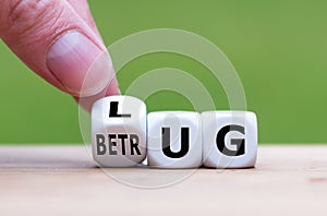 Hand turns a dice and changes the German word `LUG` `lie` in English to `Betrug` `fraud` in English.