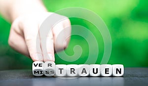 Hand turns dice and changes the German word `Misstrauen` distrust to `Vertrauen` trust.