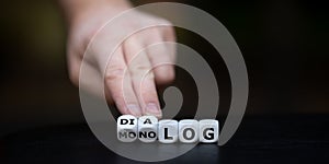 Hand turns dice and changes the German word `Monolog` monologue to `Dialog` dialogue.