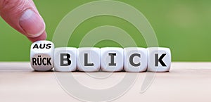 Hand turns a dice and changes the German word `RÃÂ¼ckblick` `review` in English to `Ausblick` `Outlook` in English.