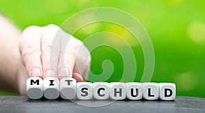 Hand turns dice and changes the German word `Schuld` guilt to `Mitschuld` joint guilt.