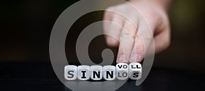 Hand turns dice and changes the German word `sinnlos` meaningless to `sinnvoll` meaningful. photo