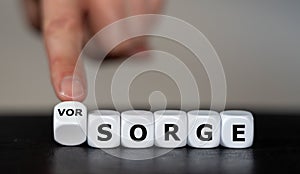 Hand turns dice and changes the German word `Sorge` concern to `Vorsorge` precaution. photo