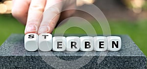 Hand turns dice and changes the German word 'Sterben' (die) to 'erben' (inherit). photo