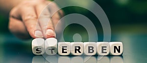 Hand turns dice and changes the German word `sterben` `die` to `erben` `inherit`. photo
