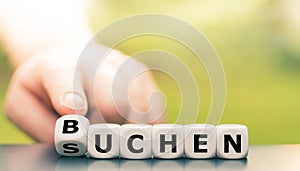 Hand turns a dice and changes the German word `suchen` `search` in English to `buchen` booking` in English. photo