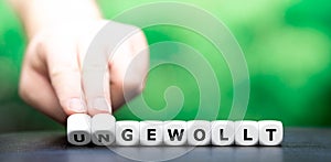Hand turns dice and changes the German word `ungewollt` unintentionally to `gewollt` intentionally.