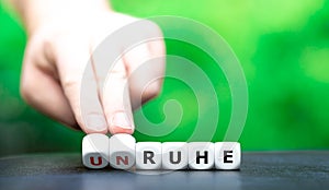 Hand turns dice and changes the German word `unruhe` restlessness to `Ruhe` silence.