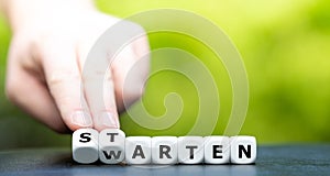 Hand turns dice and changes the German word `warten` wait to `starten` start.