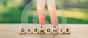 Hand turns dice and changes the German word `Ãâkonomie` `economy` to `Ãâkologie` `ecology`. photo