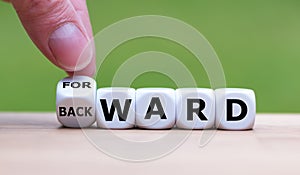 Hand turns a dice and changes the word `BACKWARD` to `FORWARD`. photo