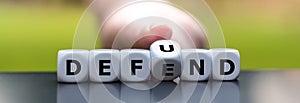 Hand turns dice and changes the word `defend` to `defund`.