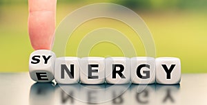 Hand turns a dice and changes the word `energy` to `synergy`, or vice versa.