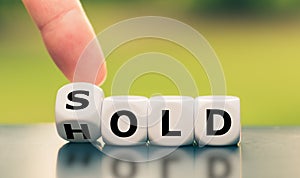 Hand turns a dice and changes the word `hold` to `sold.