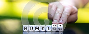 Hand turns dice and changes the word `humiliate` to `humility`.