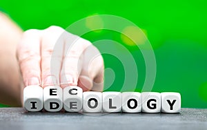Hand turns dice and changes the word `ideology` to `ecology`.