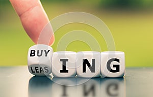 Hand turns a dice and changes the word `leasing` to `buying`, or vice versa. photo