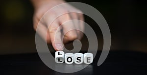 Hand turns dice and changes the word `lose` to `lose`.