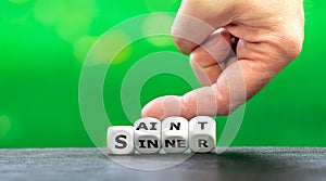 Hand turns dice and changes the word `sinner` to `saint`.