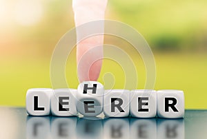Hand turns a dice and corrects a typo by changing the German word `Leerer` `empty` in English to `Lehrer` `teacher` in photo