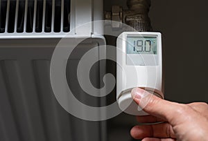 Hand turns down the temperature to 19 degrees Celsius on a electronic thermostat. Symbol for saving energy