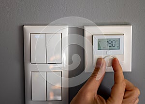 Hand turns down the temperature to 19 degrees Celsius on a electronic thermostat. Symbol for saving energy
