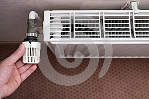 Hand turns the radiator thermostat to the minimum due to rising gas prices. Concept of energy crisis and savings. Top