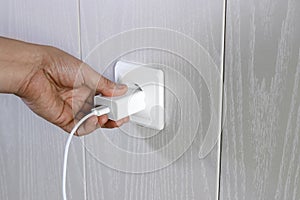 Hand turns on, turns off charger in electrical outlet on wall