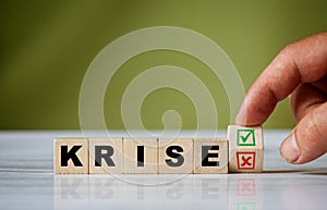 hand turns the wooden cube and changes the german word CRISE english = crisis with green positive tick check box and red reject photo