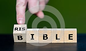 Hand turns wooden cube and changes the word bible to risible. Symbol for criticism on the bible