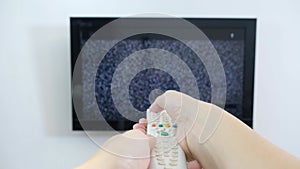 Hand with TV remote control in front of the screen with white noise on it - tuning the television channels and