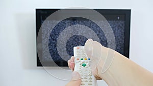 Hand with TV remote control in front of the screen with white noise on it - tuning the television channels and