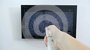 Hand with TV remote control in front of the screen with white noise on it - tuning the television channels and