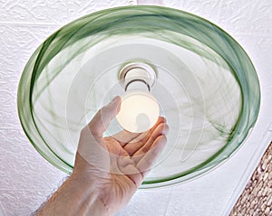 Hand twists energy-saving LED lamp on ceiling light.