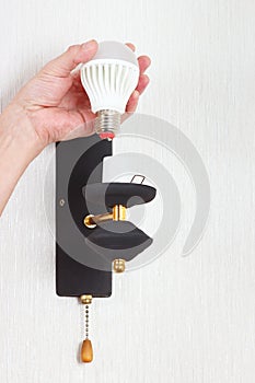 Hand twists led bulb in luminaire on white wall