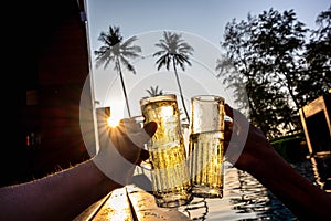 The hand of two people holding a glass of beverage and cheer each other to celebrate in the pool In the tropical garden