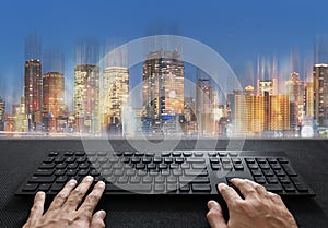 Hand typing on computer keyboard and modern buildings