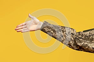 hand of Ukrainian soldier in camouflage military uniform shows palm and handshake gesture on yellow isolated background