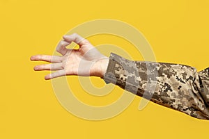 hand of Ukrainian soldier in camouflage uniform pixel shows ok and recommends on yellow isolated background, the hand of